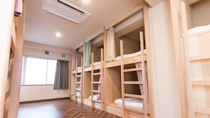 A room with bunk beds, a wooden herringbone floor, a window with curtains, and an air conditioning unit. - RED HELMET House＆Sports Bar Hiroshima - Hostel (Hiroshima)