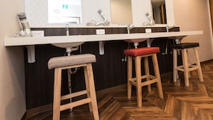 A bathroom with a wooden herringbone floor, a white sink with a mirror above it, and two wooden stools with red and black seats. - RED HELMET House＆Sports Bar Hiroshima - Hostel (Hiroshima)