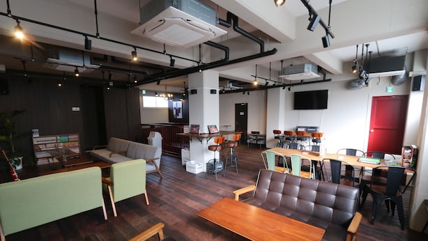 A modern interior with a wooden dining table, leather sofa, and a bar area. - RED HELMET House＆Sports Bar Hiroshima - Hostel (Hiroshima)