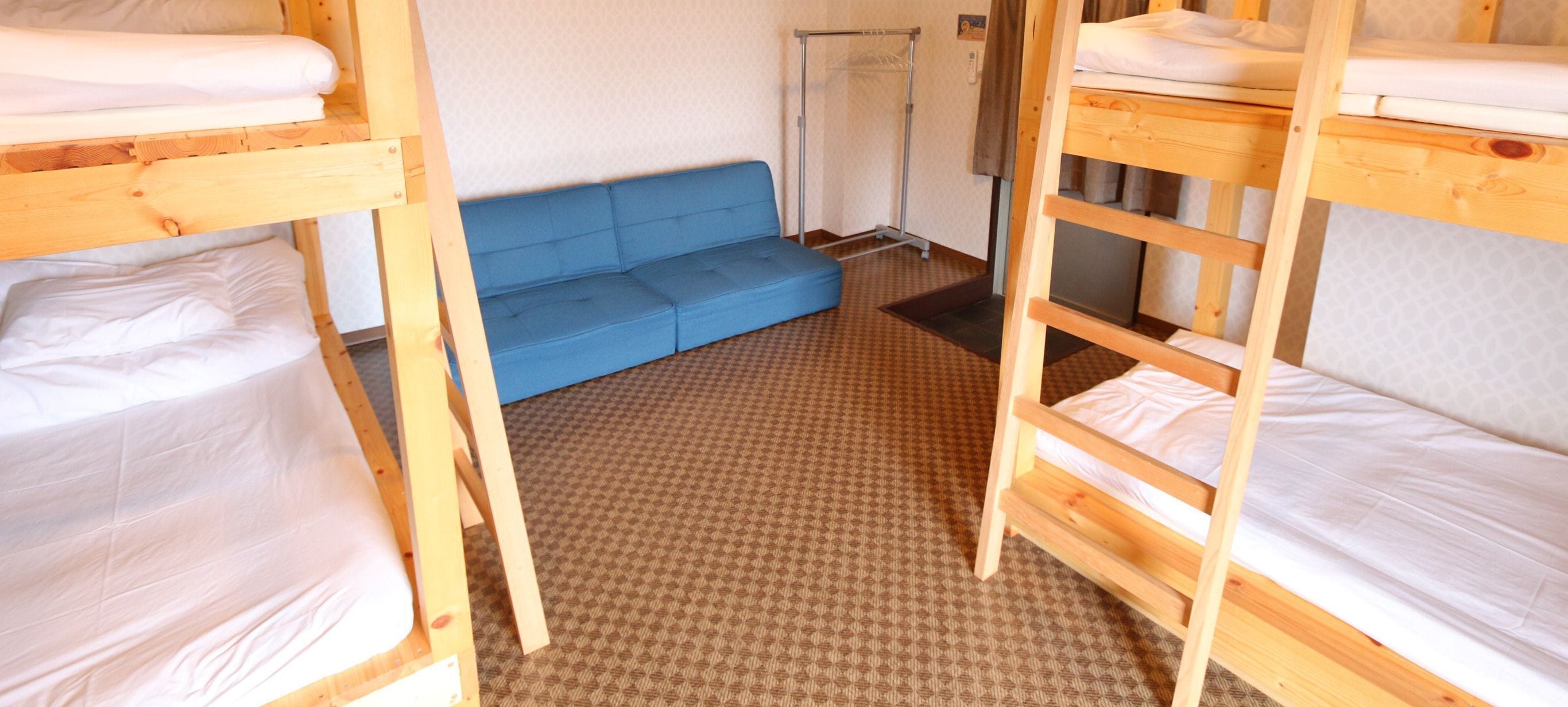 A dormitory room with bunk beds, a blue sofa, and a shower area.