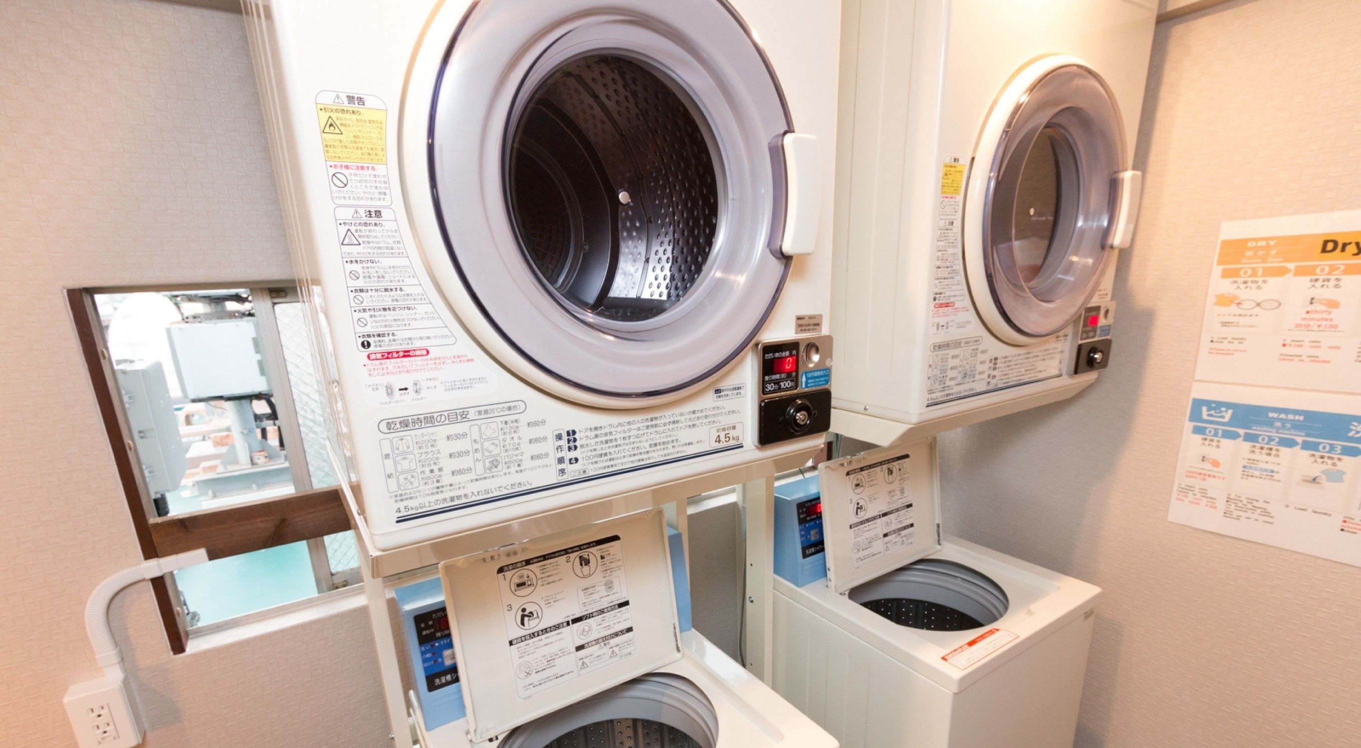 A laundry facility with multiple washing machines and dryers, including instructional labels and safety warnings.