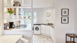 A modern kitchen with white cabinetry, a built-in washing machine, and a dining area with a white table and chairs. - Castleton , Chichester  - sleeps 2 guests  in 1 bedroom (Chichester)