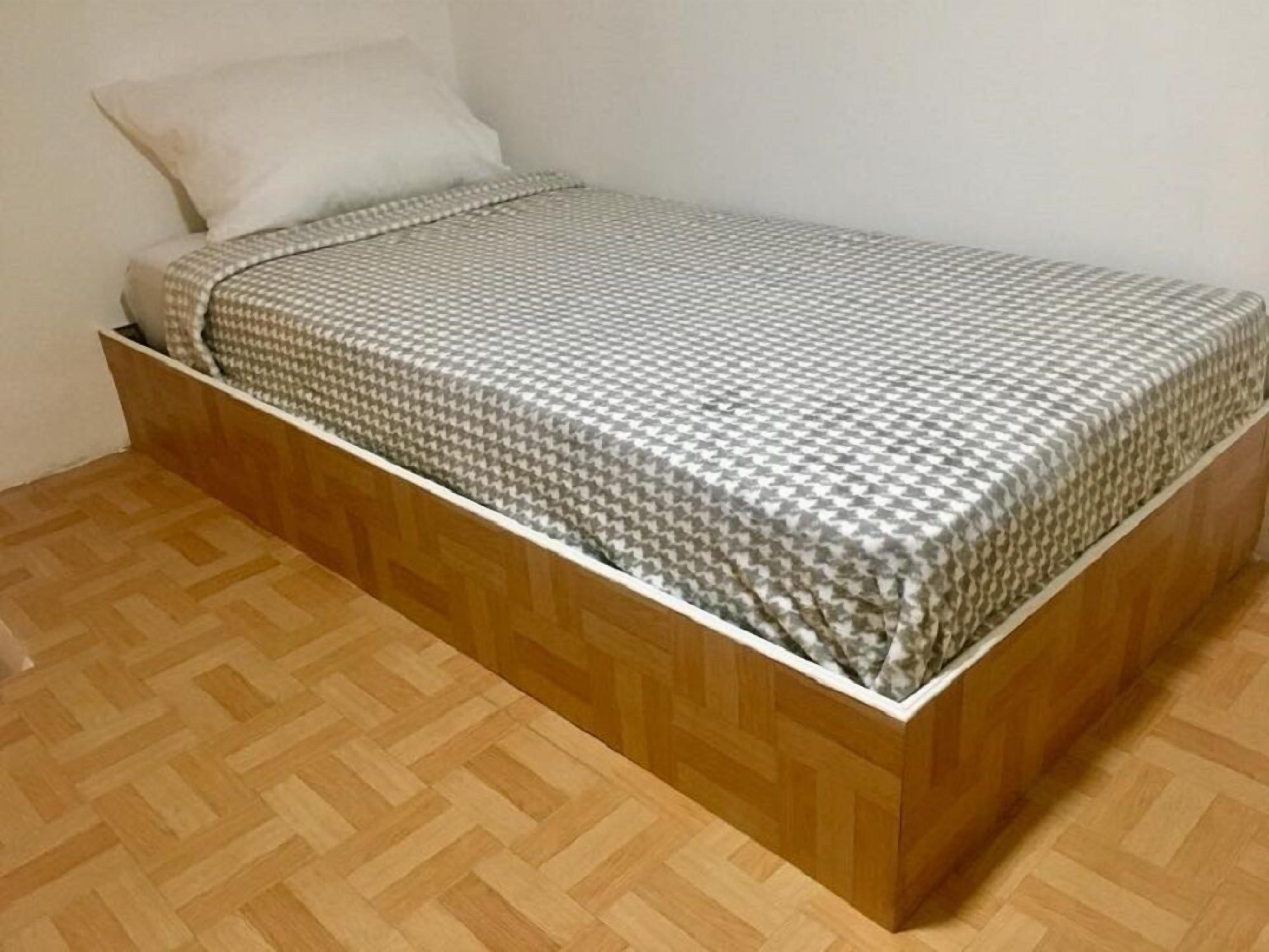 Un lit simple avec une couvre-lit à motifs, dans une pièce au plancher en bois et aux murs unis.
