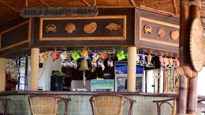 Zona de bar con sillas de mimbre, un letrero que dice 'Beer & Bullshit Area' y diversas botellas y vasos colgando.