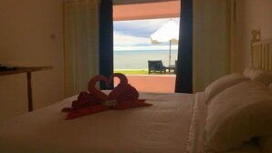 Habitación de hotel con cama, escritorio y vista a la playa a través de una puerta abierta.