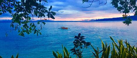 A calm lake with a boat in the distance, surrounded by lush greenery.