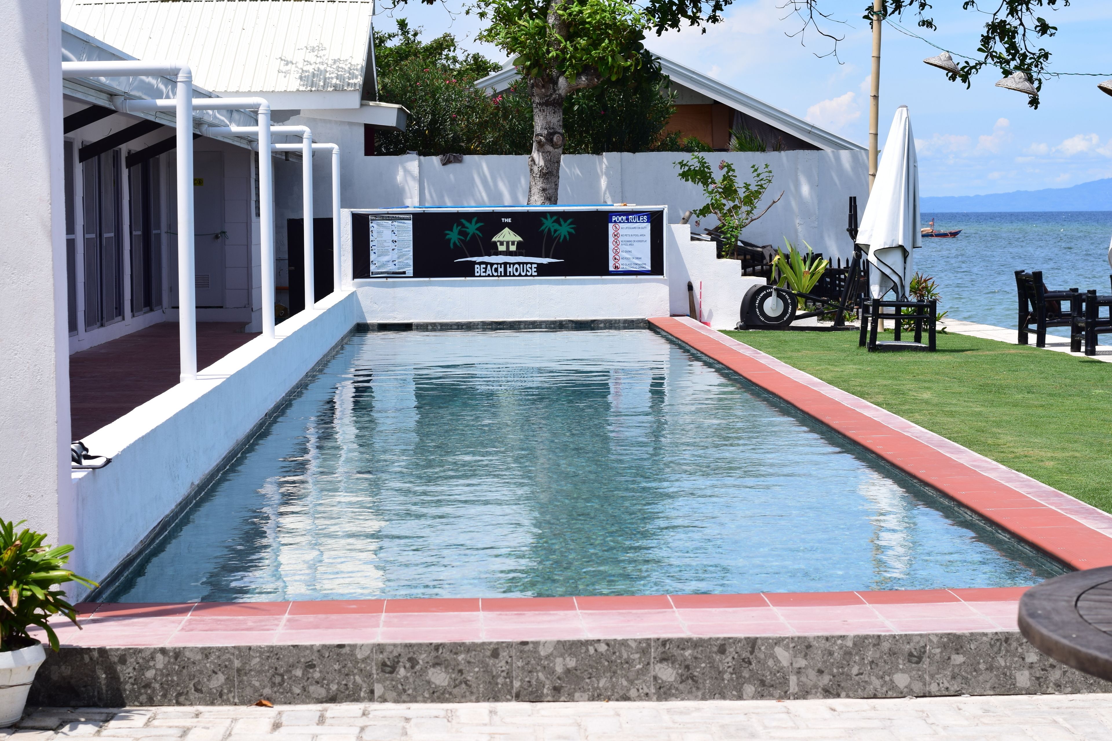 Un espace piscine agrémenté d’un panneau indiquant « The Beach House » et offrant une vue sur la mer.