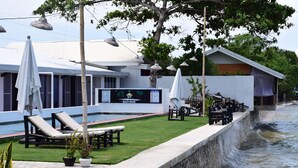Un hotel frente a la playa con sillas de descanso, piscina y un cartel que anuncia 'Beach House'.