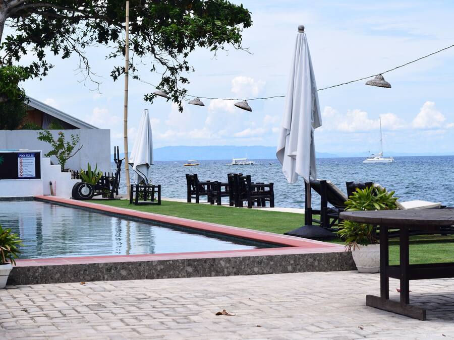 A poolside area with a view of the sea, outdoor furniture, and umbrellas.