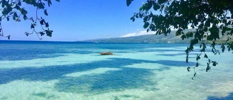 Una vista despejada de una playa con aguas turquesas poco profundas y un barco a lo lejos.