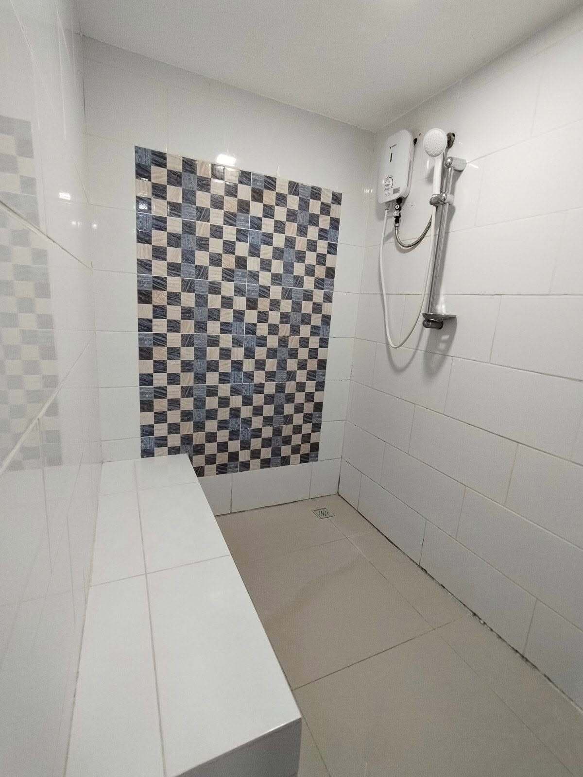A bathroom with a checkered tile wall, a shower with a handheld showerhead, and a white countertop.