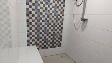 A bathroom with a checkered tile wall, a shower with a handheld showerhead, and a white countertop.