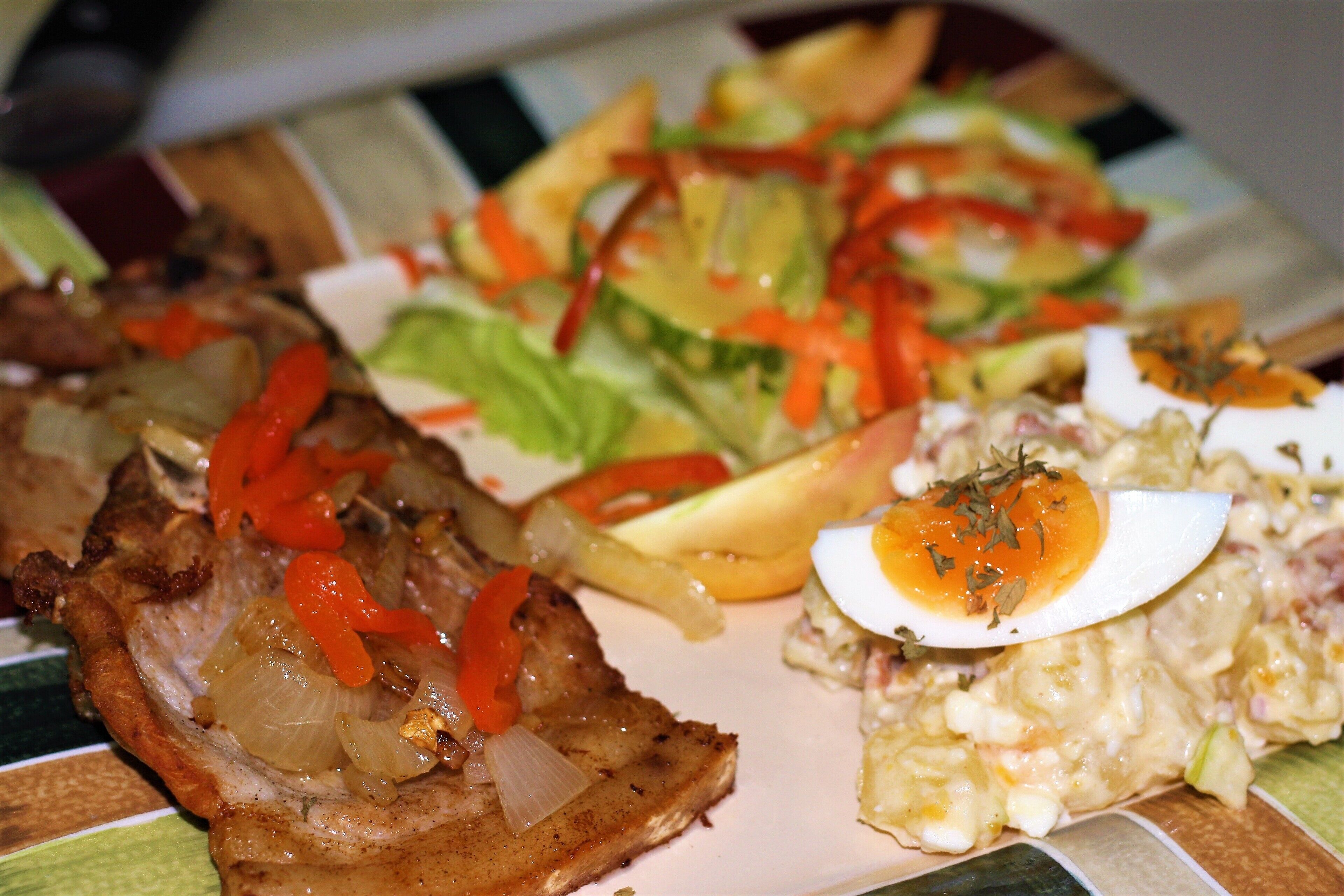 A plate with grilled meat, a salad, and a potato salad.