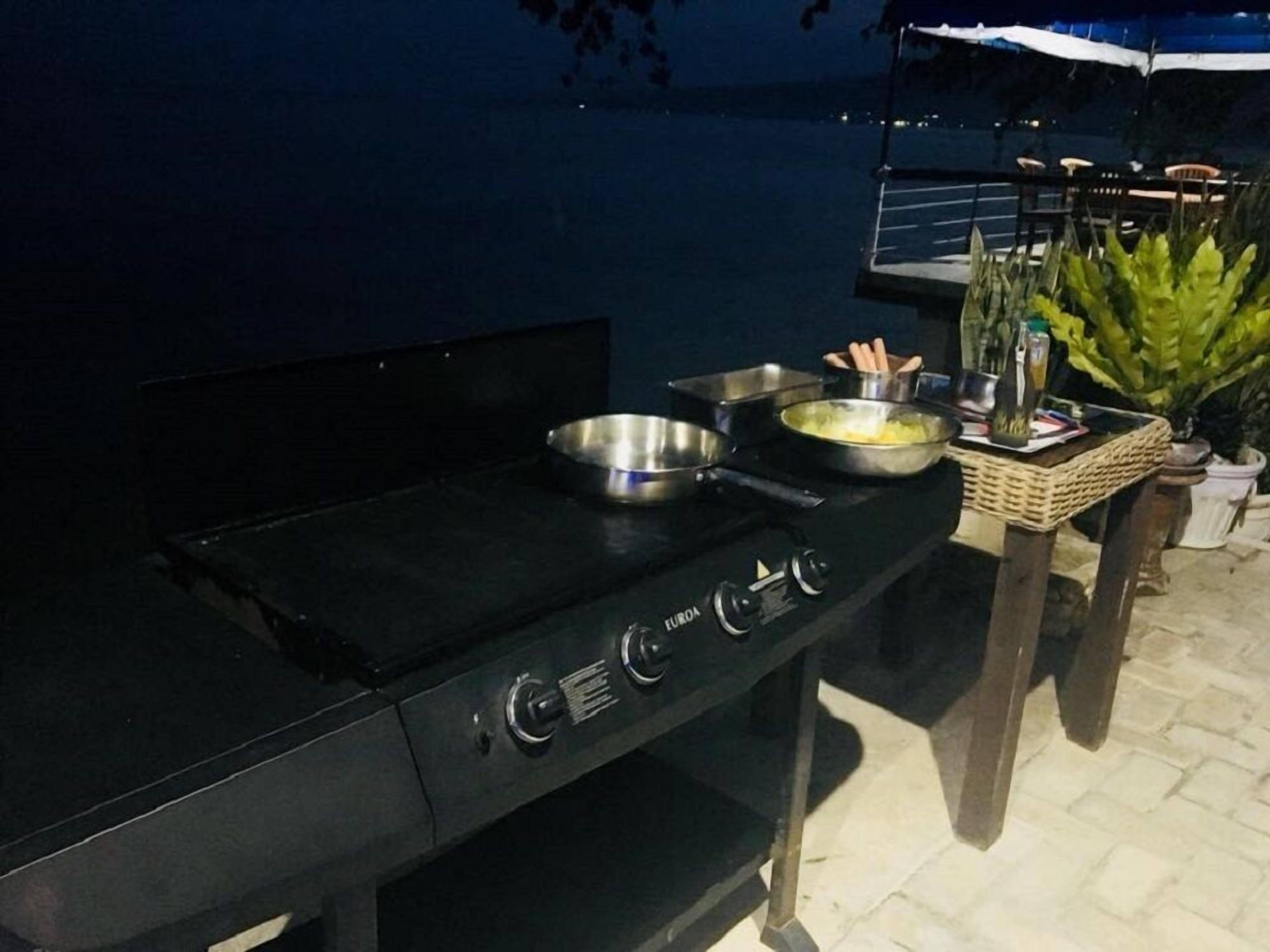 Une cuisine extérieure équipée d’une cuisinière à gaz, de casseroles et d’un panier contenant des ustensiles.