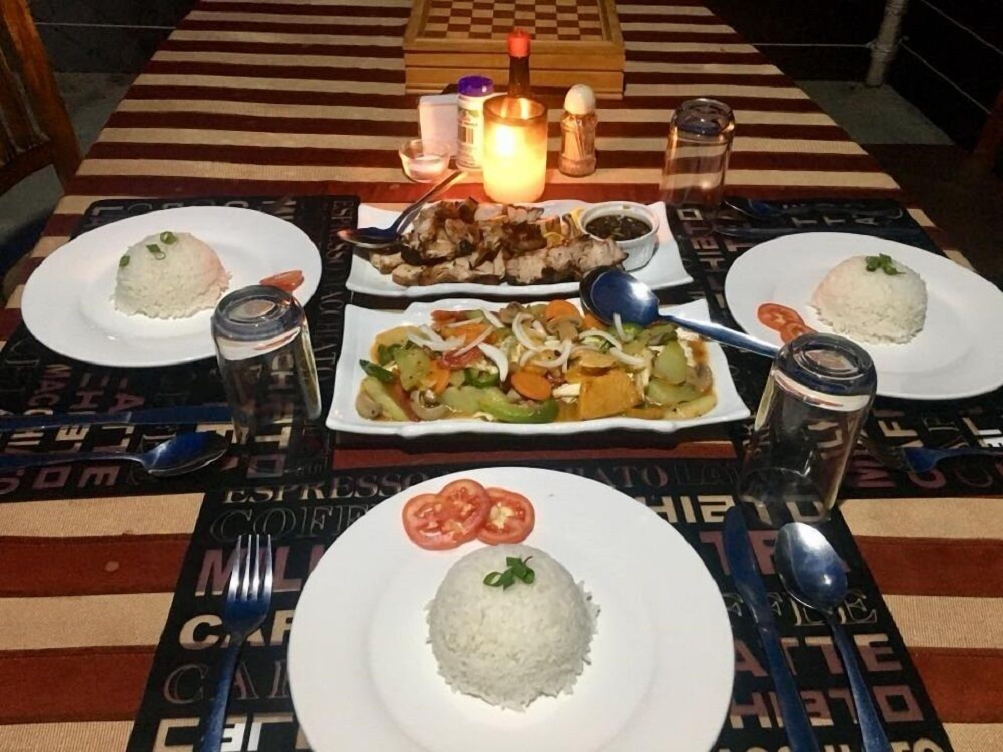 Una mesa servida con arroz, verduras y carne, acompañada de condimentos y una vela.