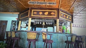 Un área de bar con un letrero que dice "BEER & BULLSHIT AREA", sillas de mimbre y piso de baldosas.