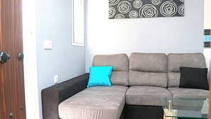 Ein modernes Wohnzimmer mit einem Ecksofa, einem Glastisch und einem an der Wand befestigten abstrakten Kunstwerk.