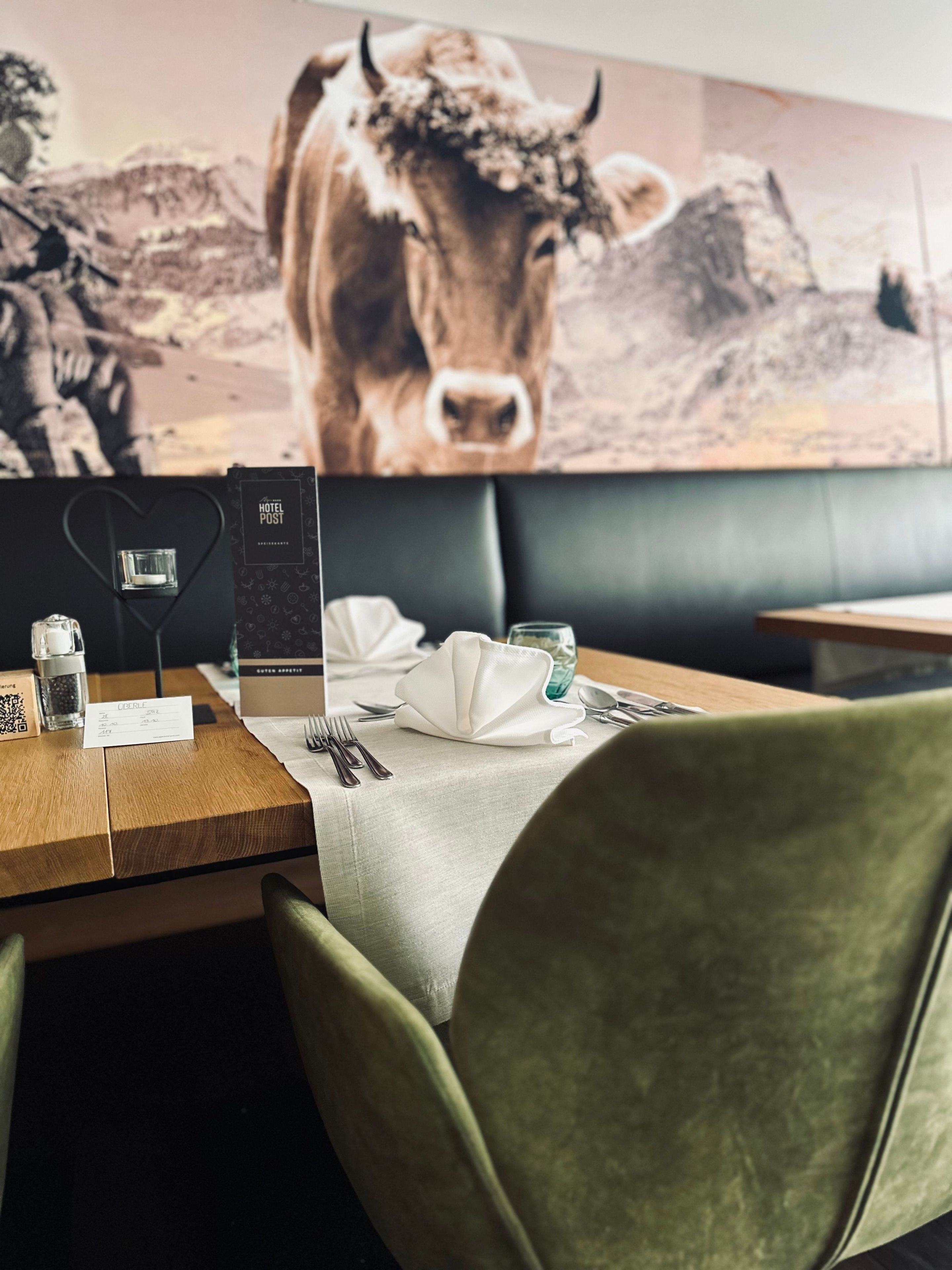 A restaurant setting with a table set for two, a menu, and a wall-mounted painting of a cow.