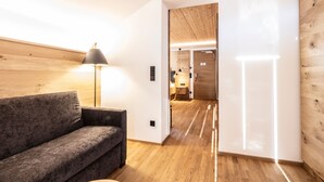 A modern interior with a wooden floor, a grey sofa, and a lamp. - Double room de luxe - alpen hotel post **** (Au)