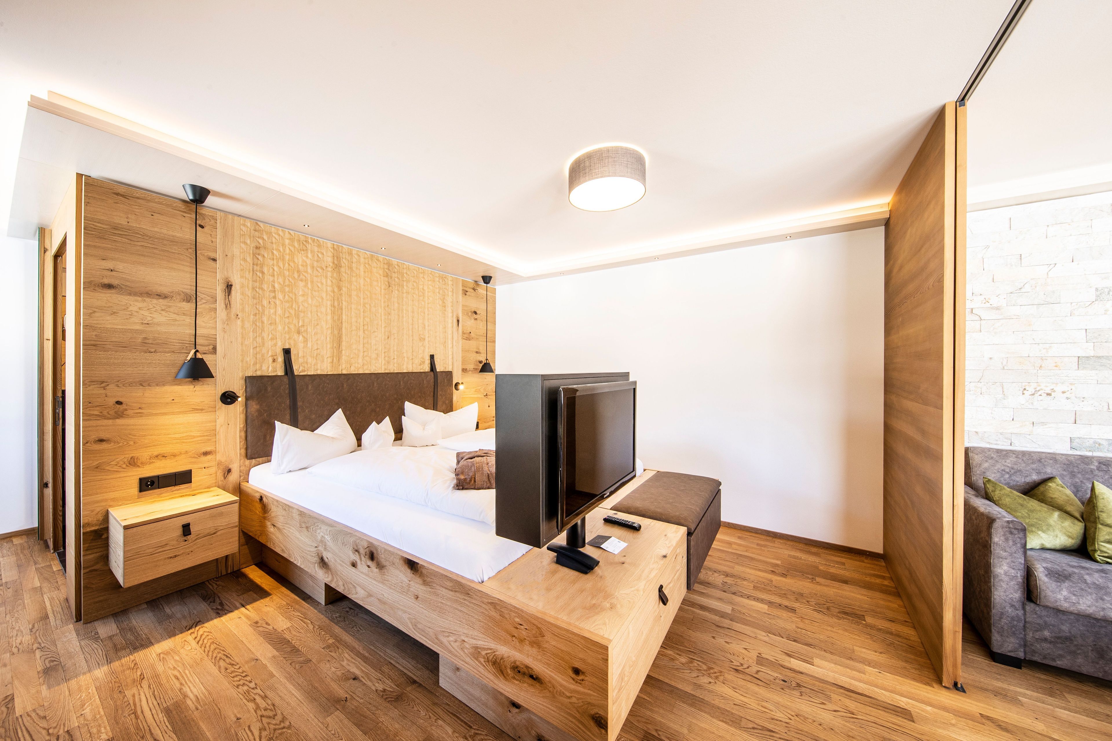 Een moderne slaapkamer met een houten bed, een televisie, een nachtkastje en een bank.