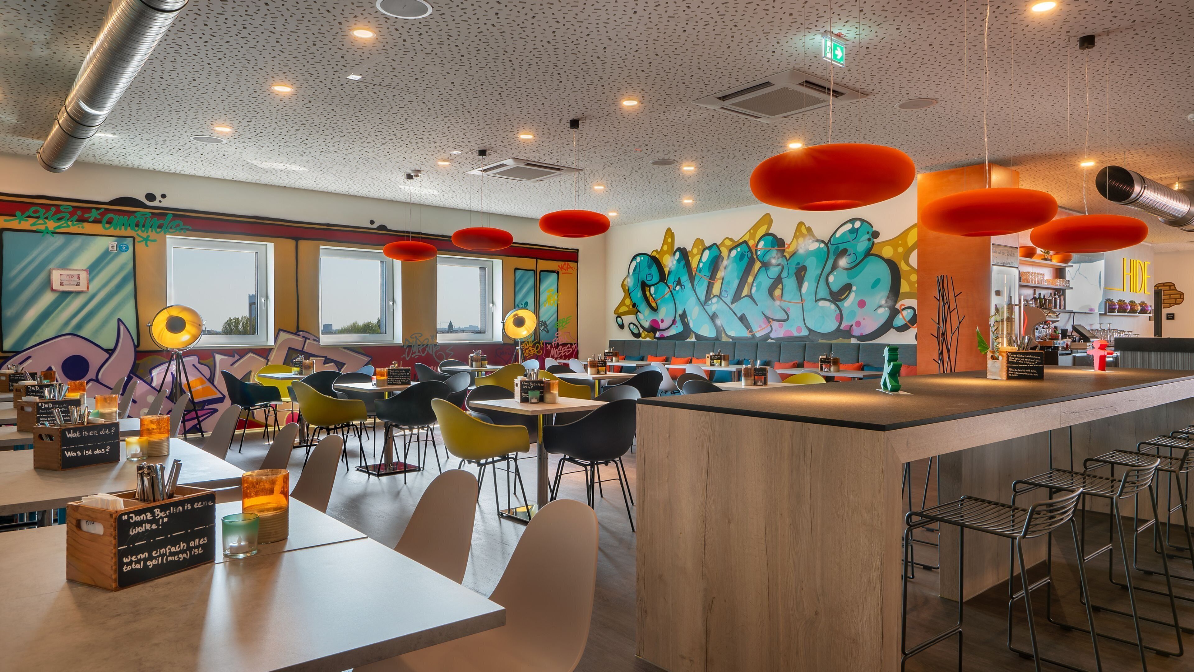 A modern cafe with colorful graffiti art, a bar area, and a variety of seating options including tables and chairs.