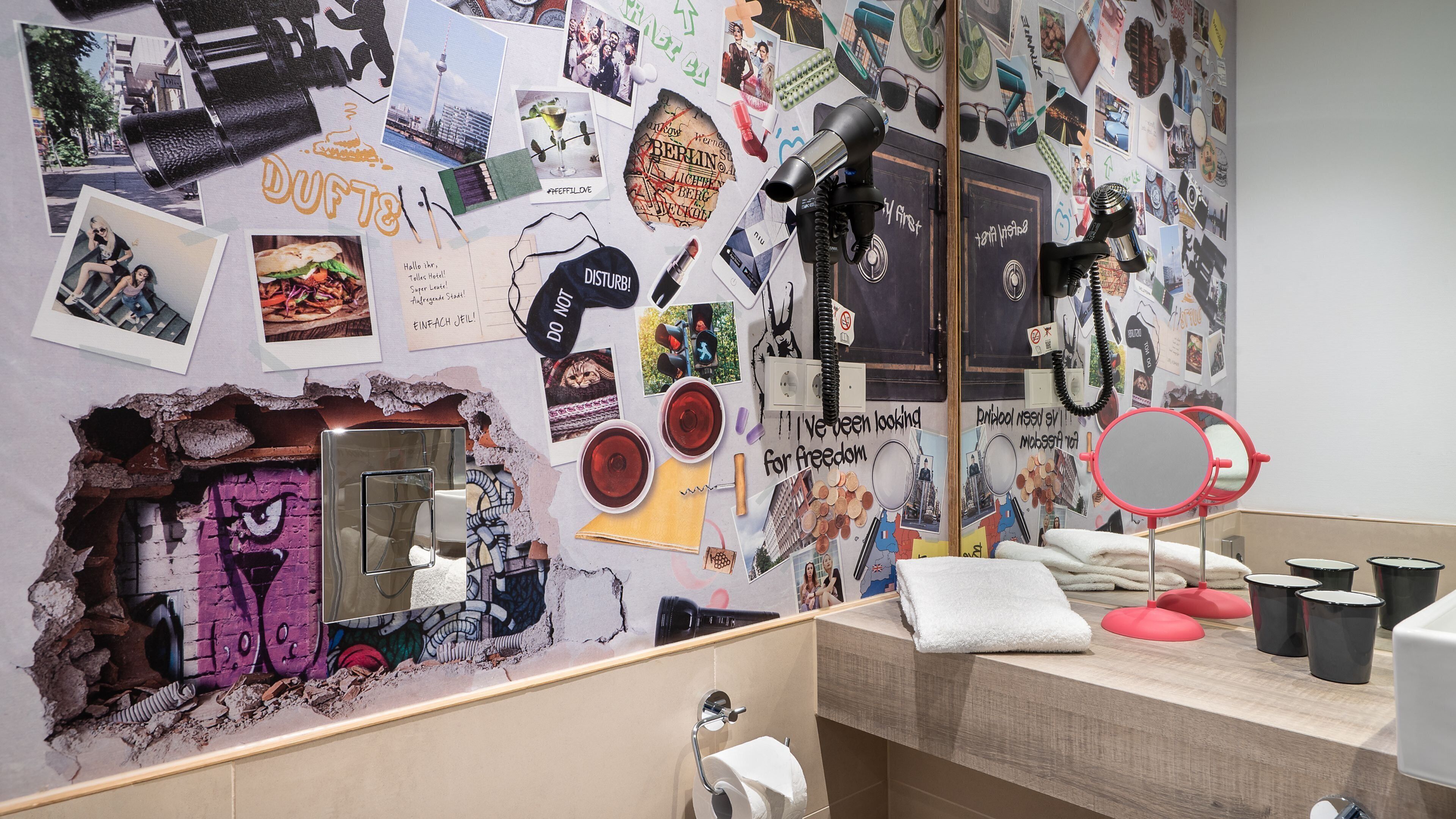 Ein Badezimmer mit einer Wand, die mit verschiedenen Fotos und Postern gestaltet ist, einem Spiegel und einem Waschbecken.