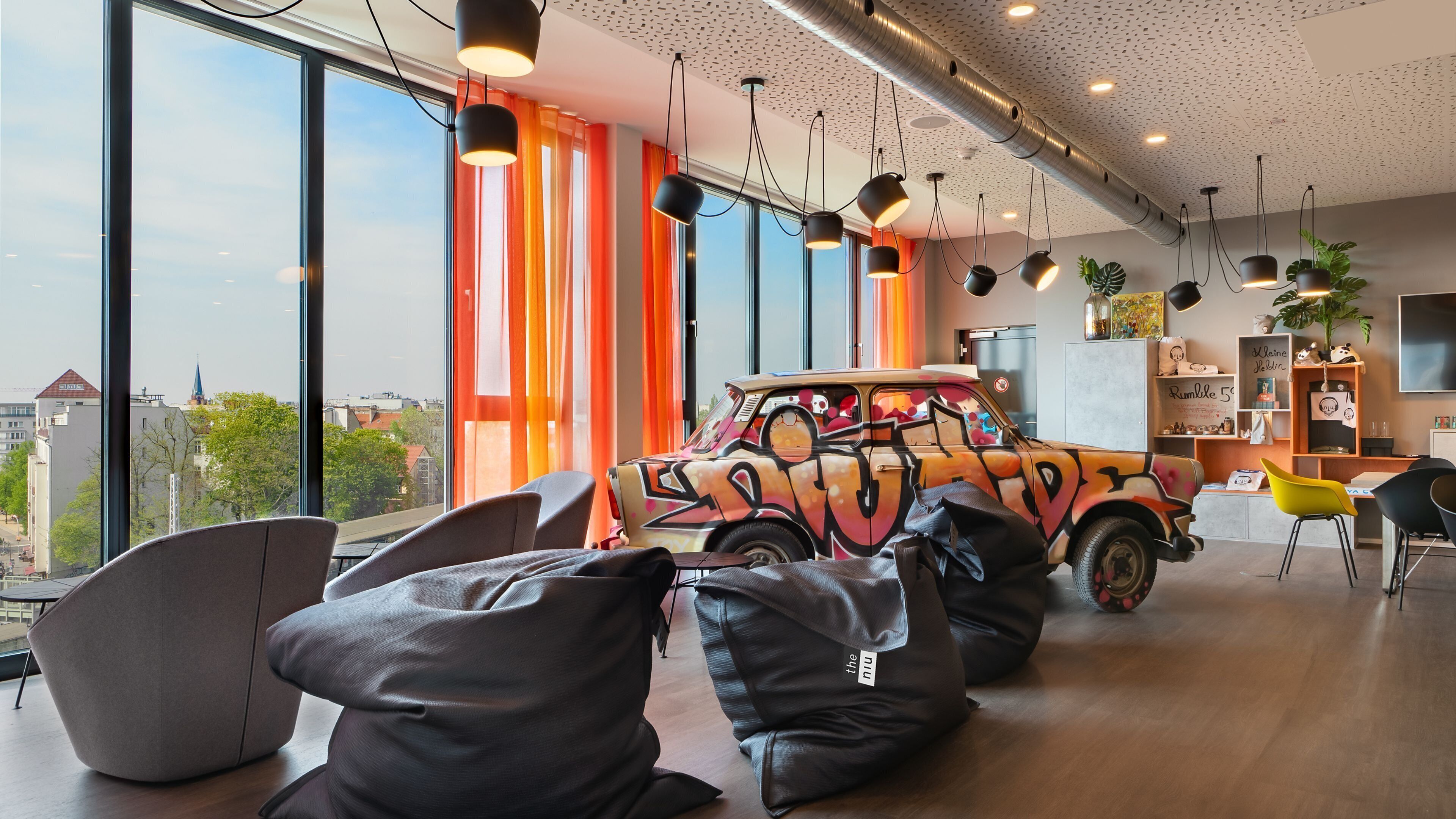 Un intérieur moderne avec de grandes fenêtres, une voiture décorée de graffitis aux couleurs vives et des espaces aménagés pour s’asseoir.