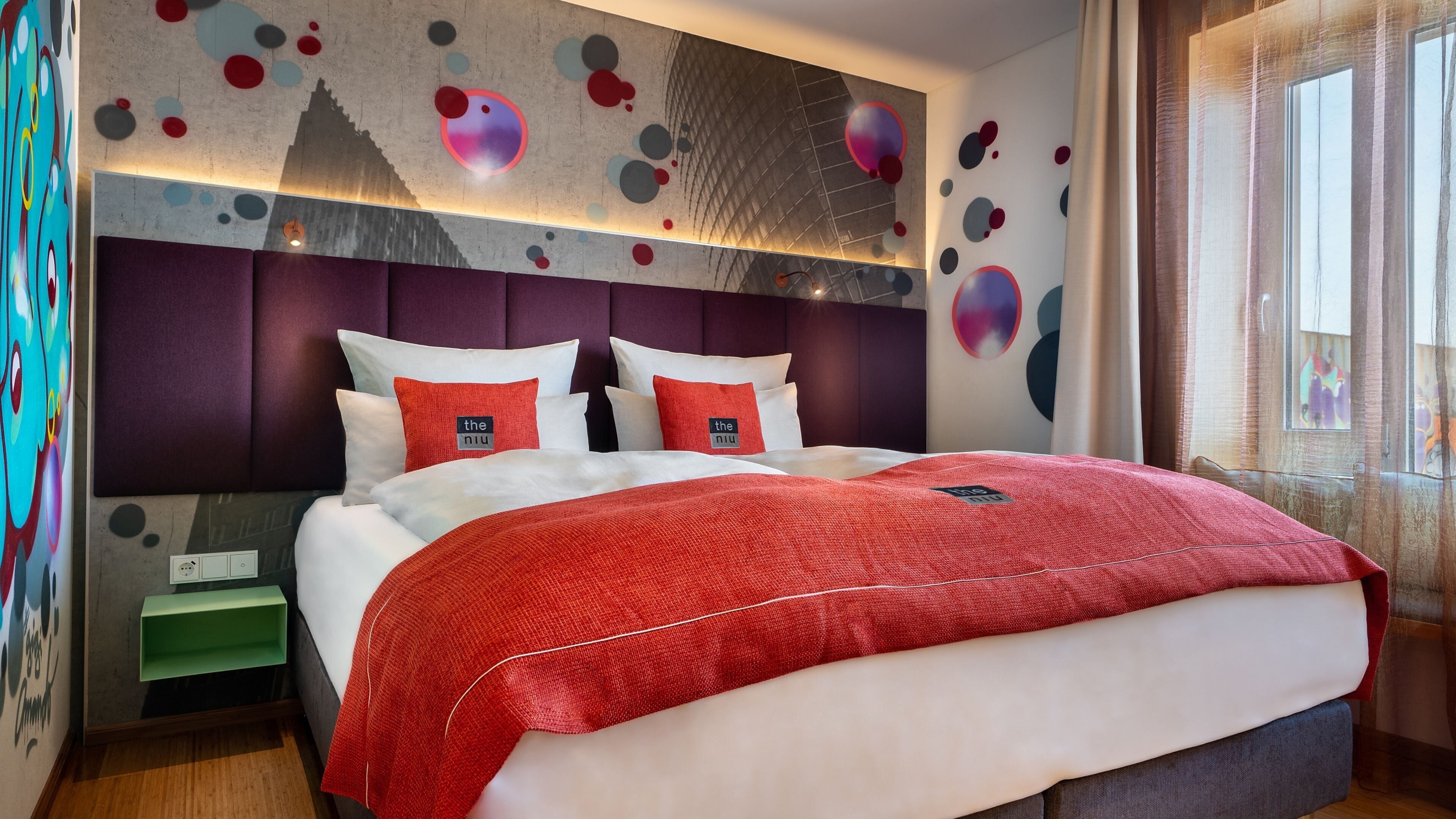 Een moderne hotelkamer met een groot bed, een hoofdbord met een geometrisch patroon, en een muur met abstracte kunst.