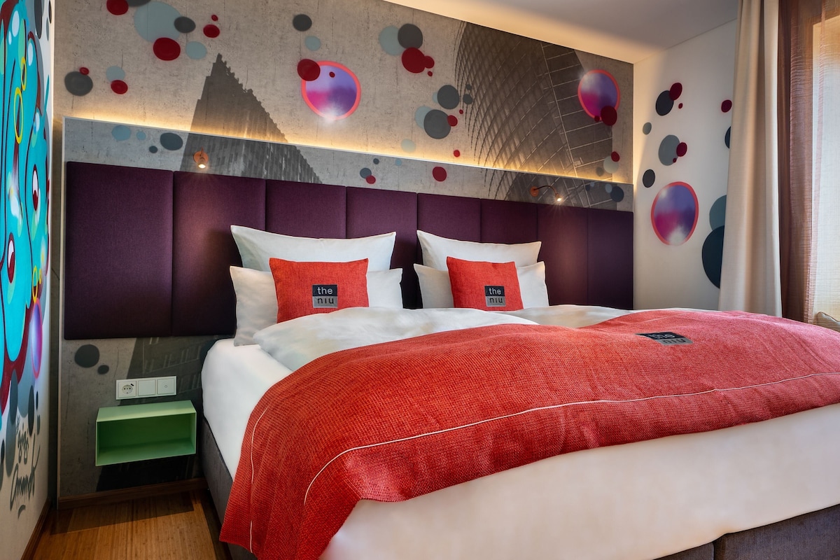 Una habitación de hotel moderna con una cama grande, un cabecero con un diseño geométrico y una pared decorada con arte abstracto.