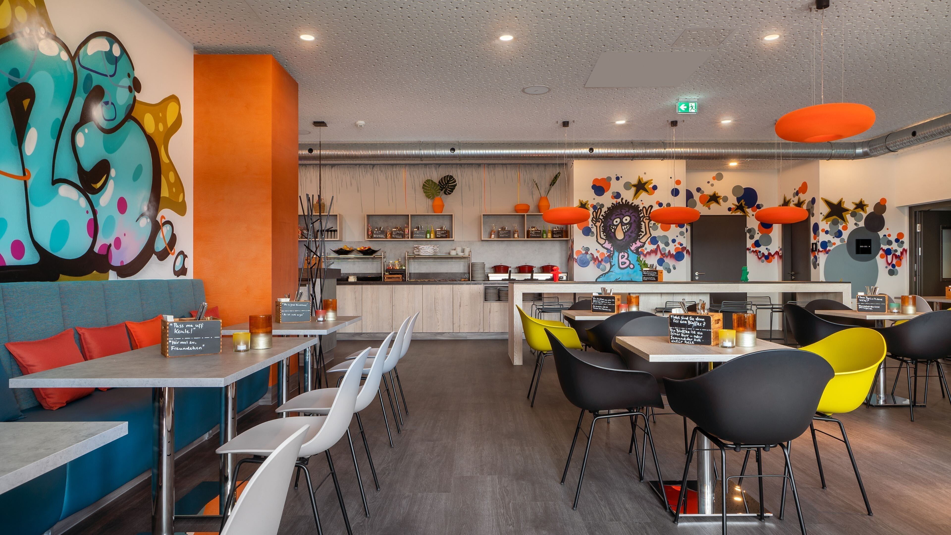 A modern restaurant with a central island, white and black chairs, and colorful wall art.