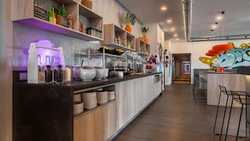 Una cocina moderna con armarios de madera, una encimera larga con distintos utensilios de cocina y un mural colorido en la pared.