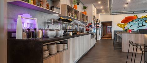 Una cocina moderna con armarios de madera, una encimera larga con distintos utensilios de cocina y un mural colorido en la pared.