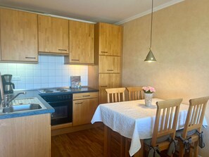 A compact kitchen with wooden cabinets, a stove, a sink, and a dining area with a table and chairs.