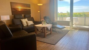 A modern living room with a sofa, armchairs, a table with a vase, and a large window with a view of the outdoors. - N18K (BC.a5) - Stranddomicil Steiner (Büsum)