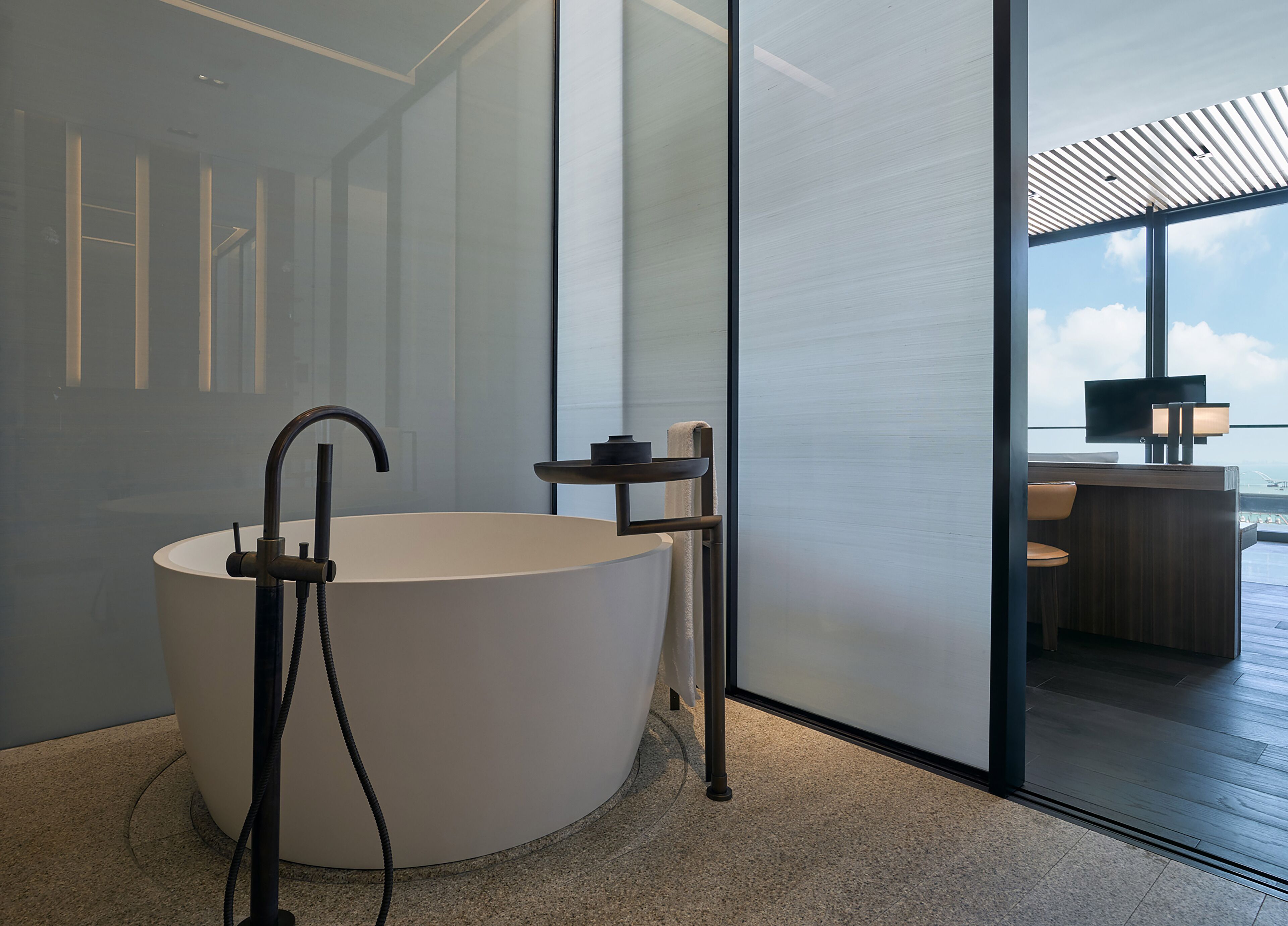 A modern bathroom with a freestanding bathtub, a towel rack, and a glass partition.