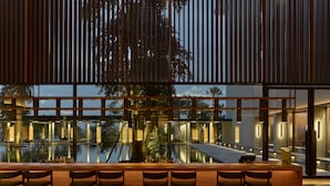 Zona de bar con vista a una piscina y árboles, con listones de madera y taburetes.