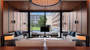 Um lobby de hotel moderno com uma ampla área de estar, uma televisão de tela plana e vista para o exterior do edifício.