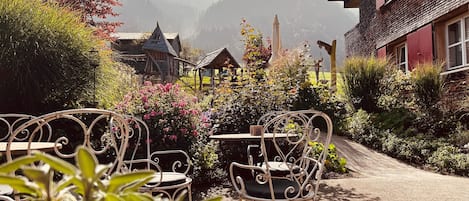A garden with metal chairs and tables, a wooden structure, and a mountain backdrop.