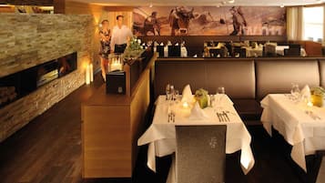 A restaurant with tables set for dining, a fireplace, and a large mural on the wall.