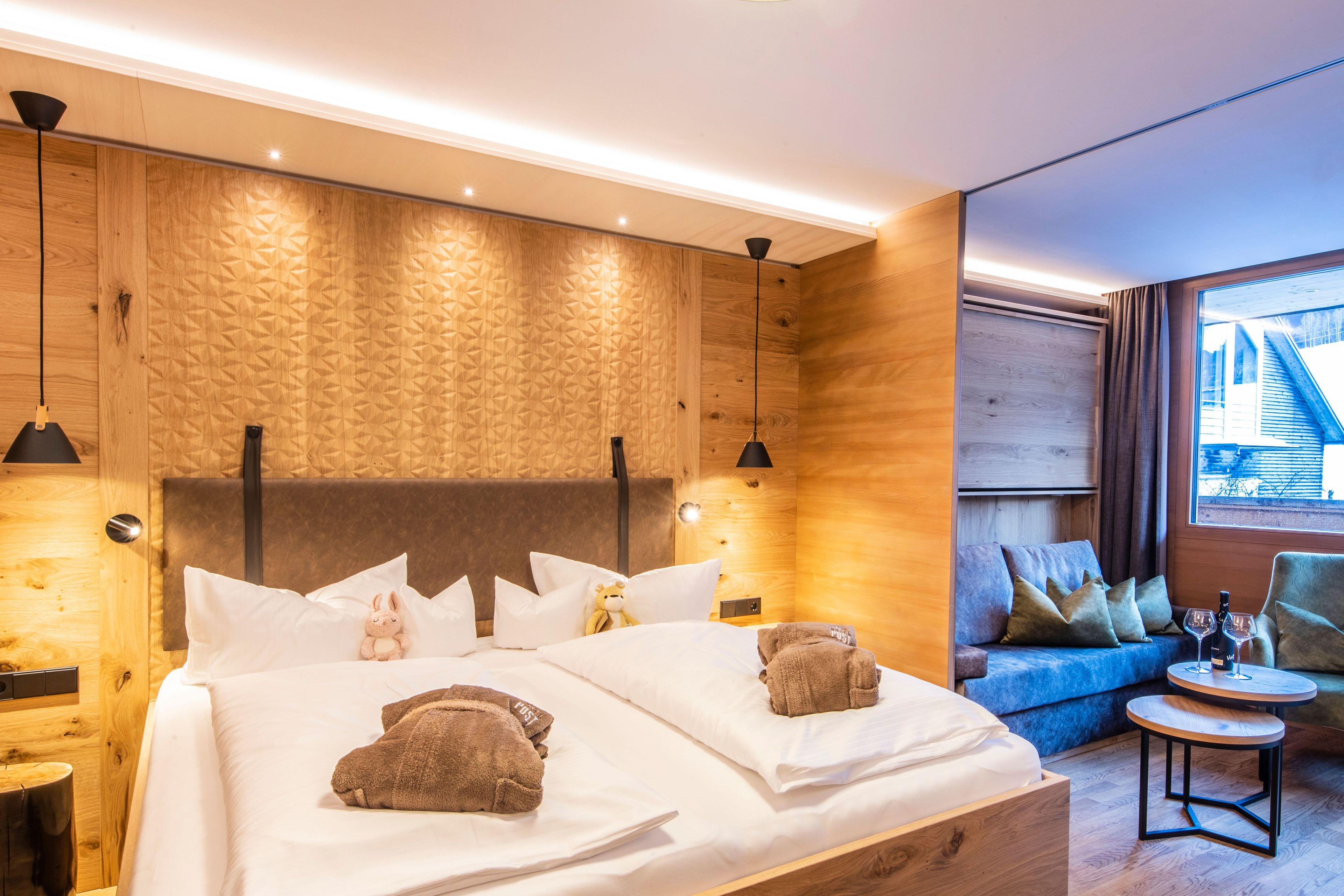 Une chambre d’hôtel moderne avec un grand lit, un canapé, une petite table et une fenêtre donnant sur un beau paysage.