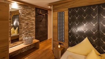 A modern room with a wooden floor, a bed with yellow pillows, a bench with a basket, a mirror, and a wall with a deer pattern.