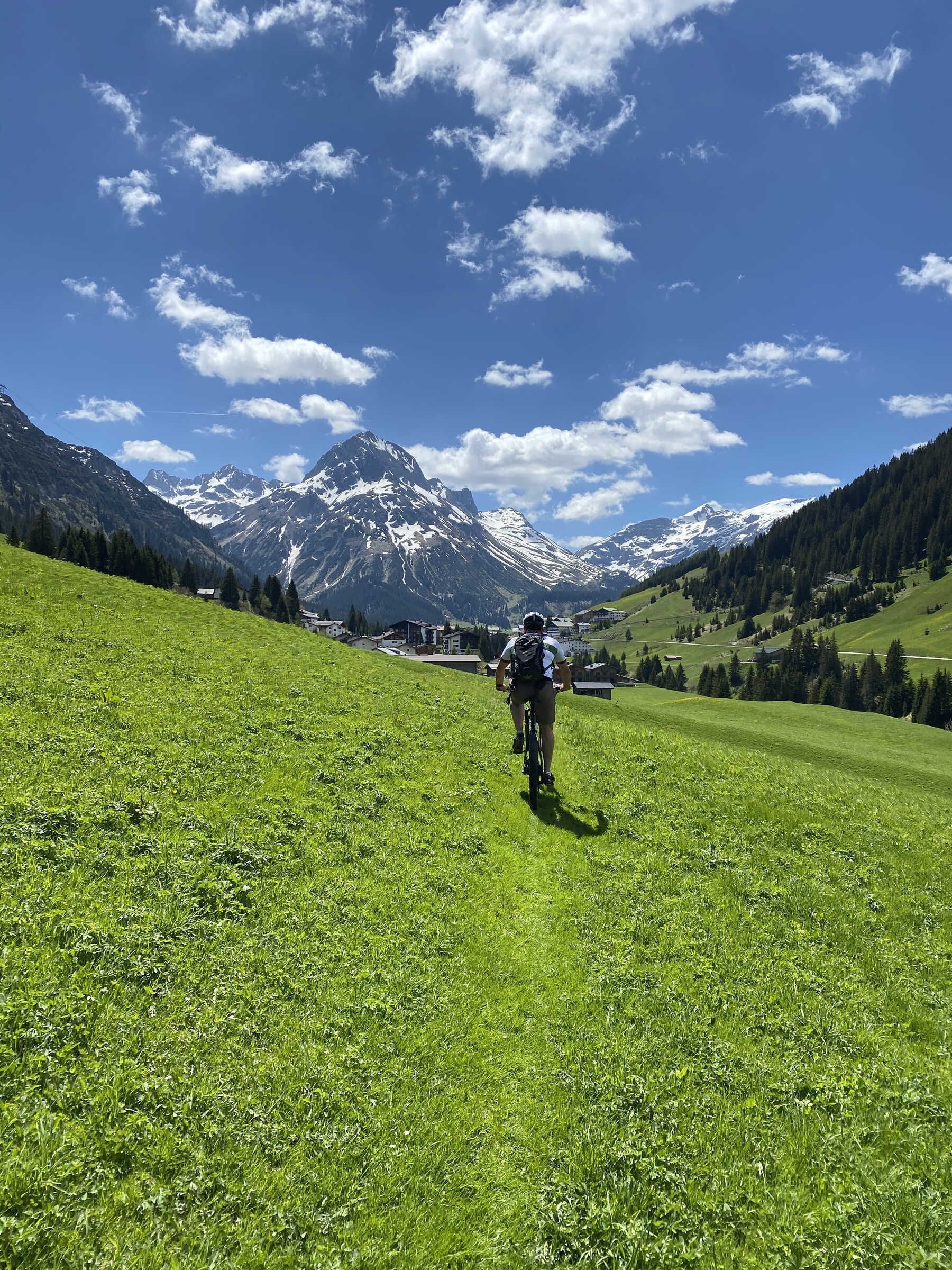 A cyclist on a grassy hill with mountains in the background.