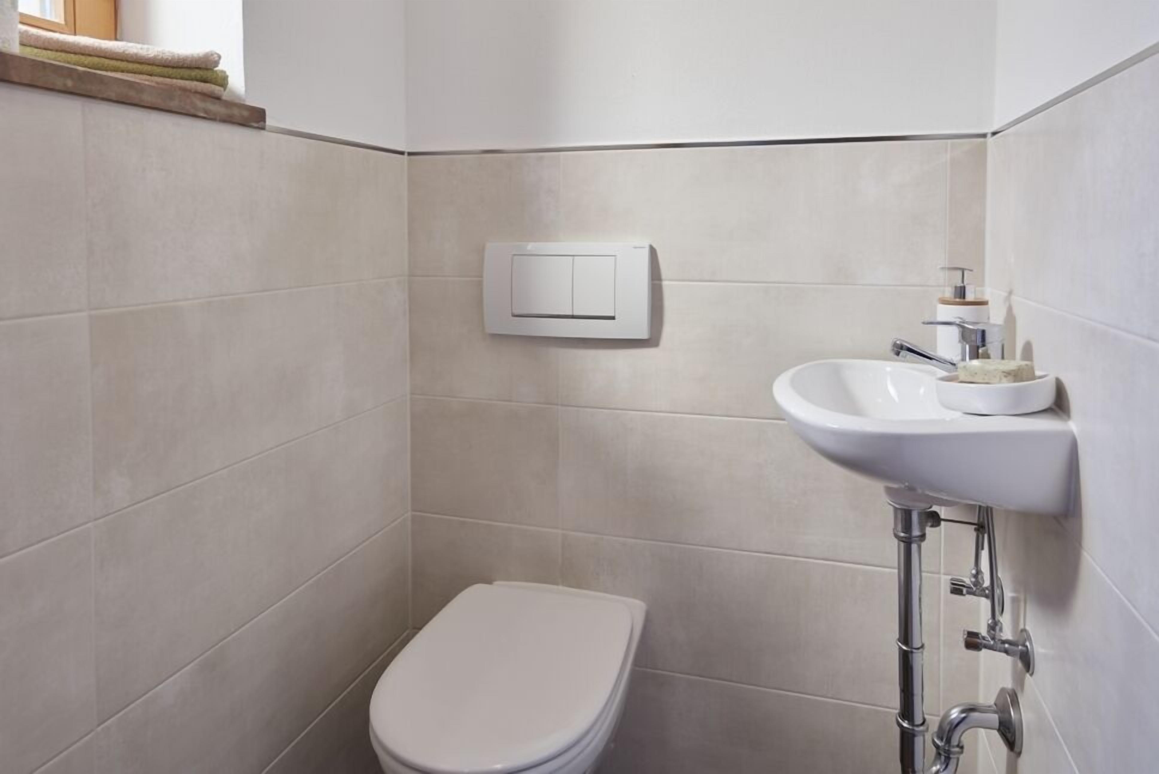 Un baño con inodoro blanco, lavamanos montado en la pared y un perchero para toallas.