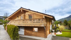 Un chalet en bois doté d’un balcon, d’une petite fenêtre et d’un jardin agrémenté de plantes en pot.