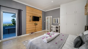 Une chambre moderne avec balcon, un téléviseur fixé au mur en bois, une armoire et un lit agrémenté de serviettes et de fleurs.