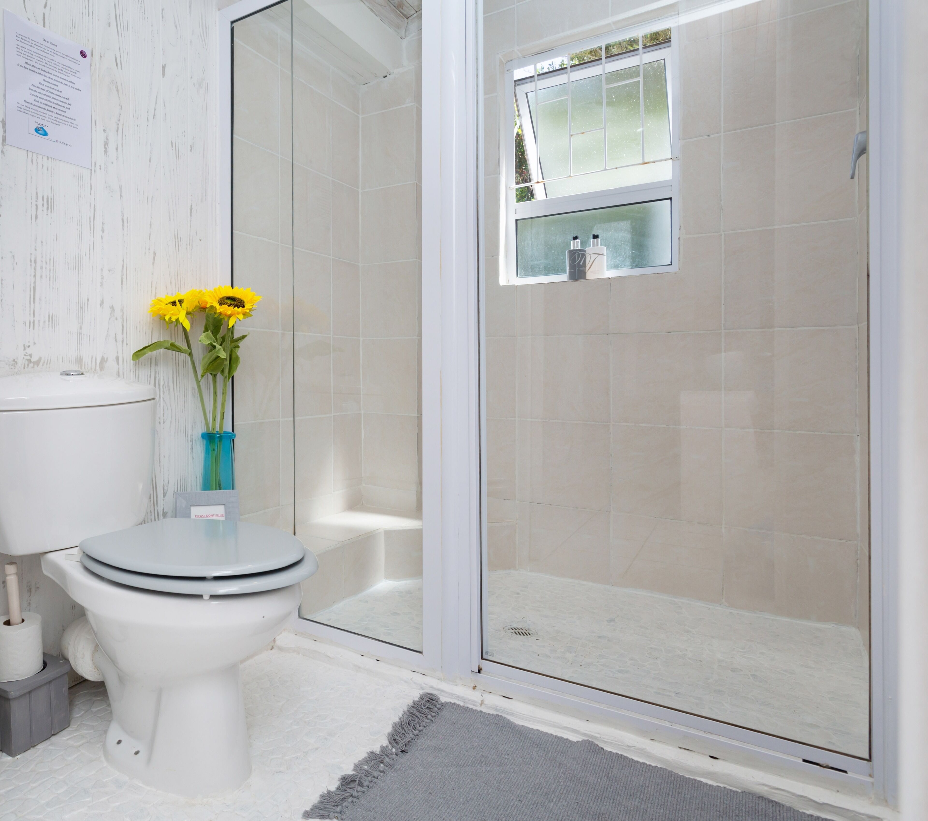 Une salle de bain avec des toilettes, une douche à parois de verre et un vase rempli de fleurs jaunes.