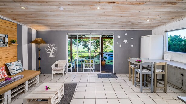 Une pièce chaleureuse avec un plafond en bois, une grande porte-fenêtre coulissante donnant sur un espace extérieur, une petite table avec des chaises et un banc.