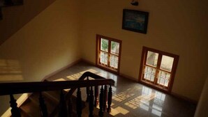 Una escalera conduce a una habitación con dos ventanas, un cuadro en la pared y una barandilla de madera.