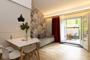 A modern living room with a white sofa, a dining table with chairs, and a large window with curtains. - Little Suite Apartments (Dresden)