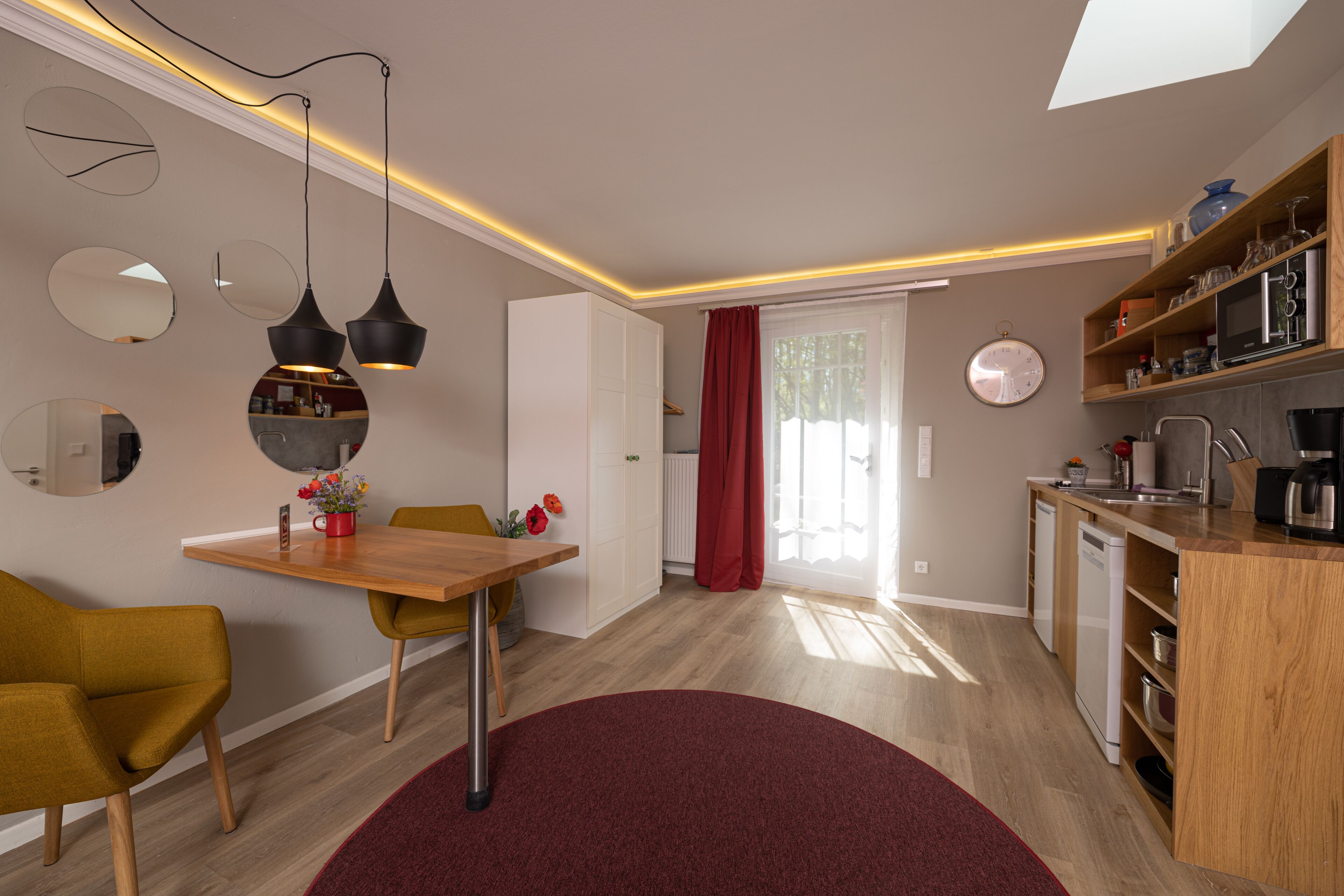 A modern kitchen with wooden cabinets, a dining area with a table and chairs, and a red rug.